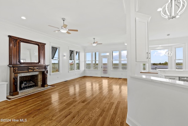 unfurnished living room featuring light hardwood / wood-style floors, ornamental molding, and ceiling fan with notable chandelier