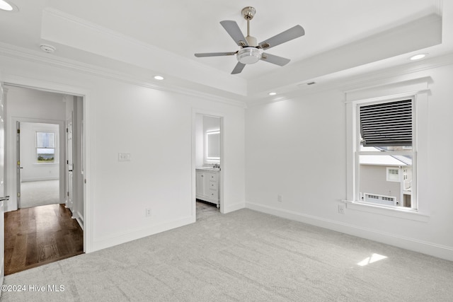 unfurnished bedroom with ensuite bathroom, ceiling fan, a raised ceiling, light colored carpet, and crown molding