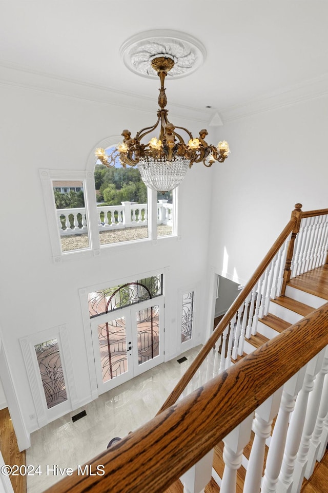 staircase featuring french doors, a notable chandelier, and ornamental molding