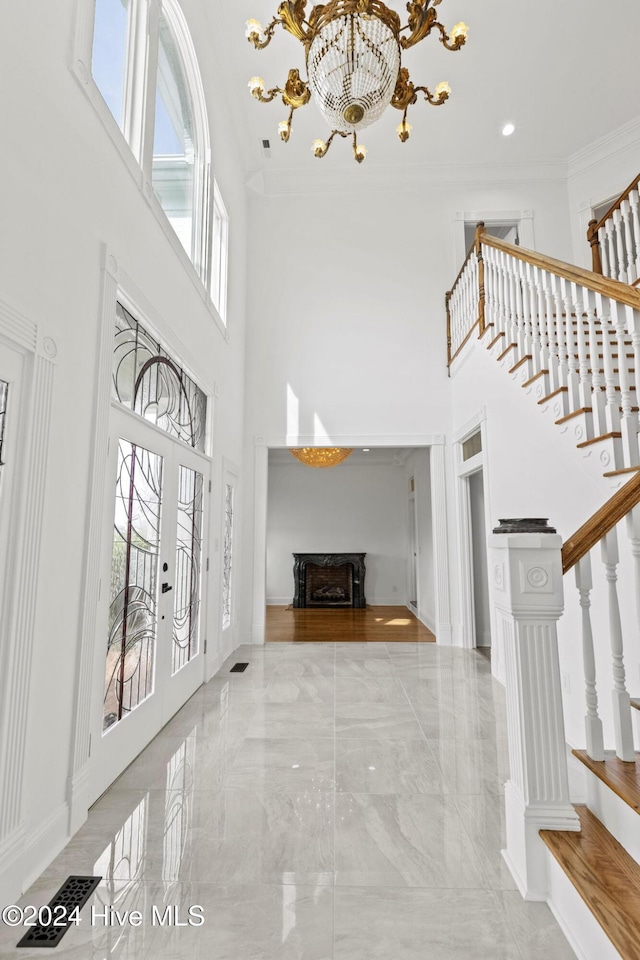 foyer with a high ceiling, french doors, ornamental molding, and a chandelier