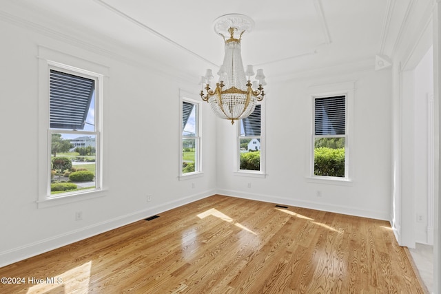 empty room featuring hardwood / wood-style flooring, ornamental molding, and an inviting chandelier