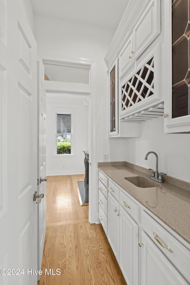 kitchen featuring light hardwood / wood-style flooring, white cabinets, light stone counters, and sink