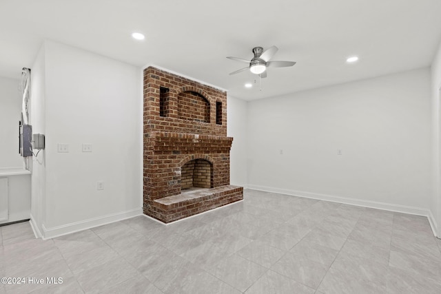 unfurnished living room featuring ceiling fan and a brick fireplace