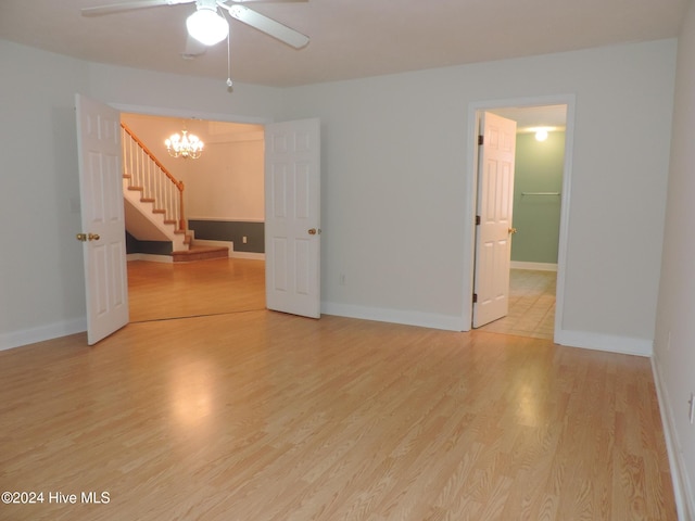 spare room with hardwood / wood-style floors and ceiling fan with notable chandelier