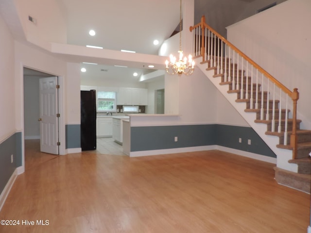 unfurnished living room with a chandelier, high vaulted ceiling, and light hardwood / wood-style flooring