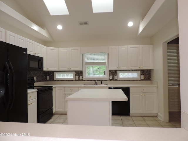 kitchen featuring white cabinetry, lofted ceiling with skylight, a center island, and black appliances