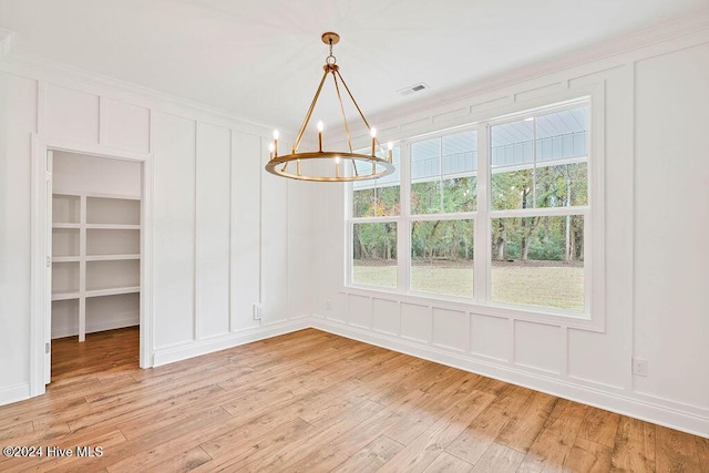 unfurnished dining area with crown molding, light hardwood / wood-style floors, and a notable chandelier