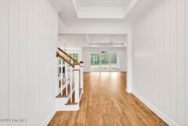 corridor featuring light wood-type flooring, ornamental molding, a raised ceiling, an inviting chandelier, and wood walls