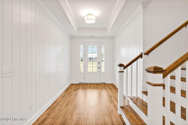 entrance foyer featuring a raised ceiling, ornamental molding, and light wood-type flooring