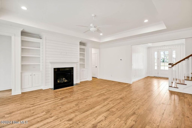 unfurnished living room featuring built in shelves, ceiling fan, light wood-type flooring, and crown molding