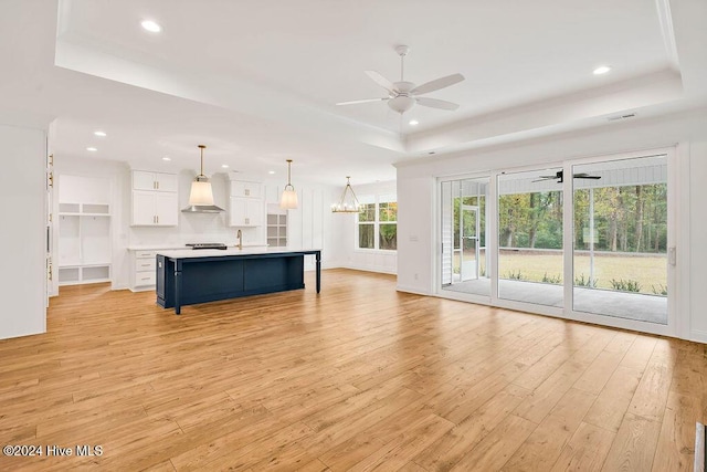 unfurnished living room with a tray ceiling, light hardwood / wood-style floors, and ceiling fan with notable chandelier