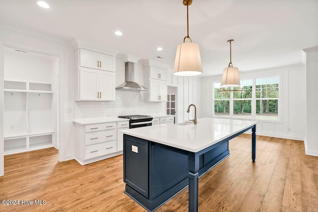 kitchen featuring white cabinetry, black stove, wall chimney range hood, light hardwood / wood-style floors, and decorative light fixtures