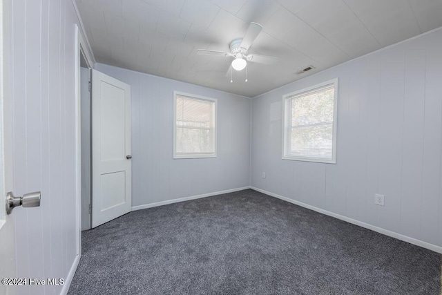 unfurnished room featuring ceiling fan, dark carpet, and a wealth of natural light