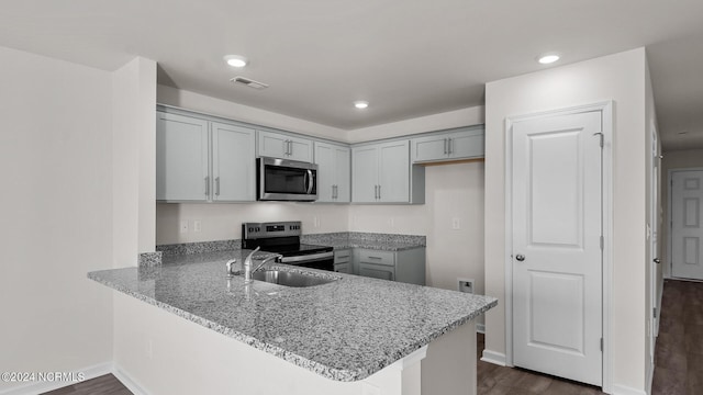 kitchen with kitchen peninsula, appliances with stainless steel finishes, dark hardwood / wood-style flooring, light stone counters, and gray cabinets