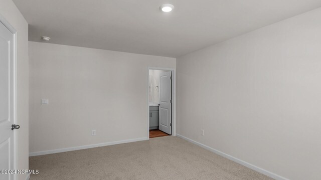 unfurnished bedroom with ensuite bath and light colored carpet