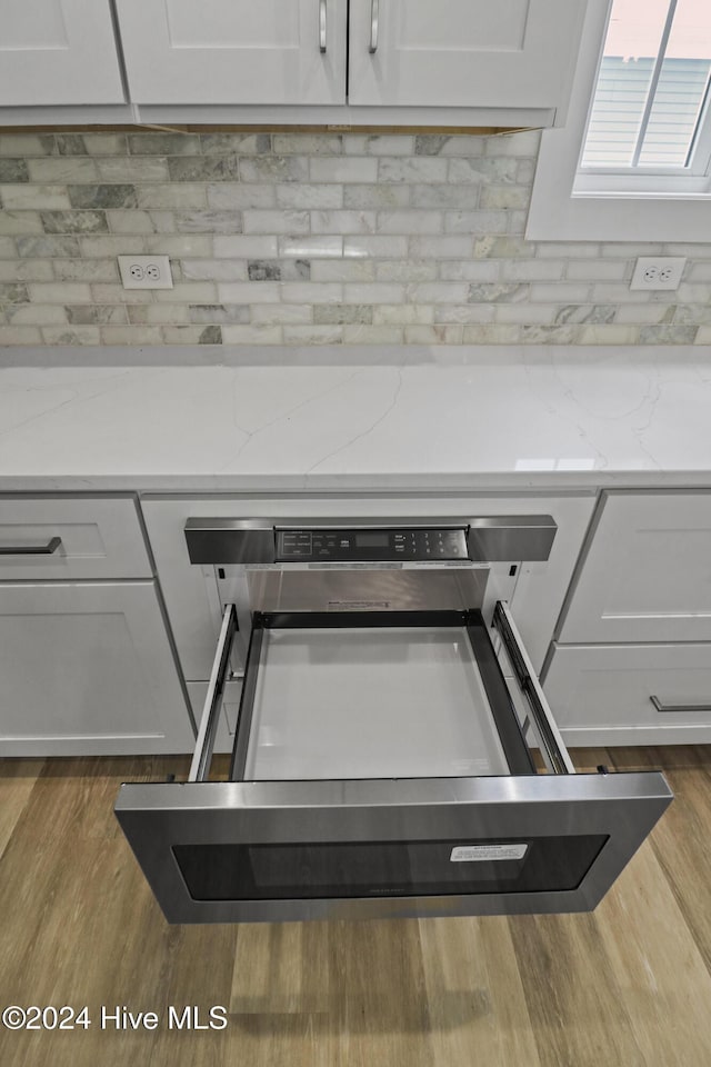 kitchen featuring wall chimney exhaust hood, hanging light fixtures, appliances with stainless steel finishes, white cabinets, and hardwood / wood-style flooring