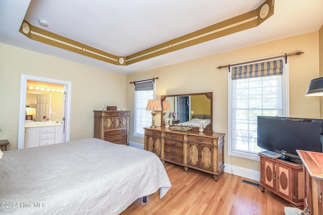 bedroom with light hardwood / wood-style floors, a raised ceiling, and ensuite bath