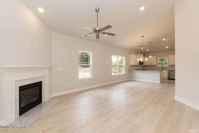 unfurnished living room featuring a premium fireplace, ceiling fan, and light hardwood / wood-style floors