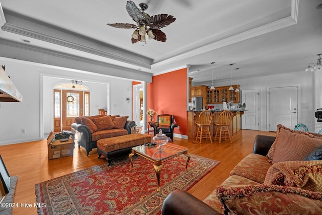 living room with ceiling fan with notable chandelier, light hardwood / wood-style floors, a raised ceiling, and ornamental molding