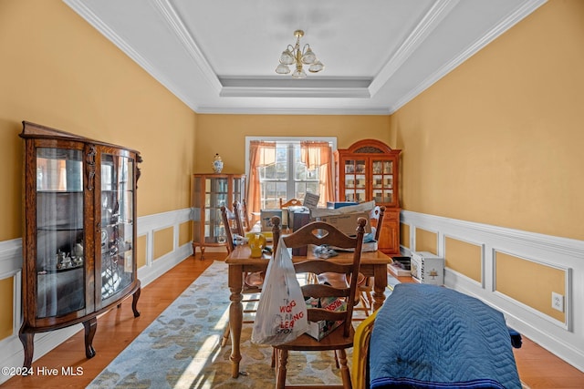 dining area with french doors, a notable chandelier, light hardwood / wood-style floors, a tray ceiling, and ornamental molding