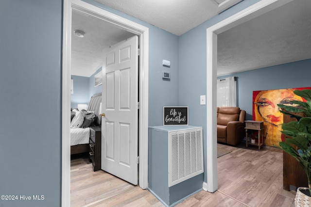 hall with light hardwood / wood-style floors and a textured ceiling