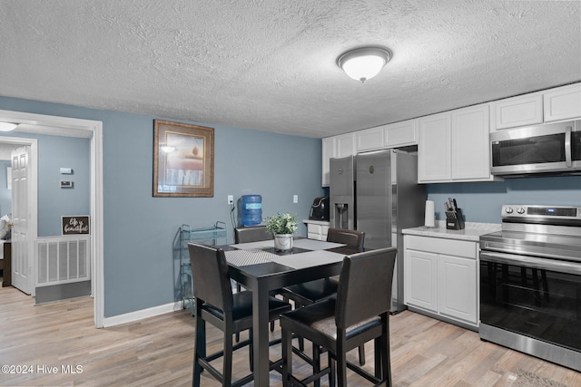 kitchen featuring white cabinets, light wood-type flooring, a textured ceiling, and appliances with stainless steel finishes