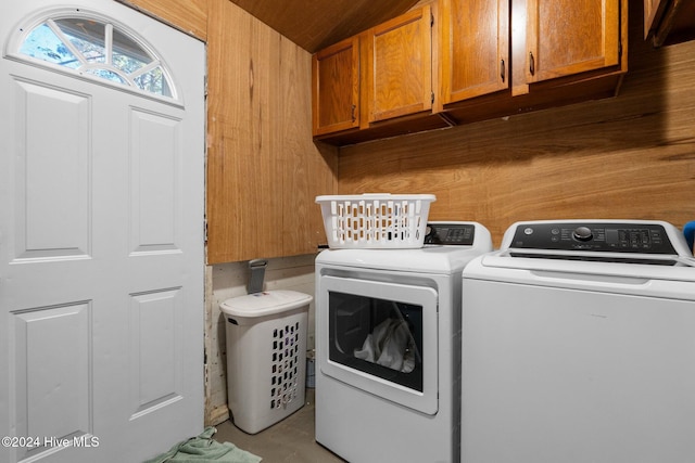 laundry area with wood walls, cabinets, and washing machine and dryer