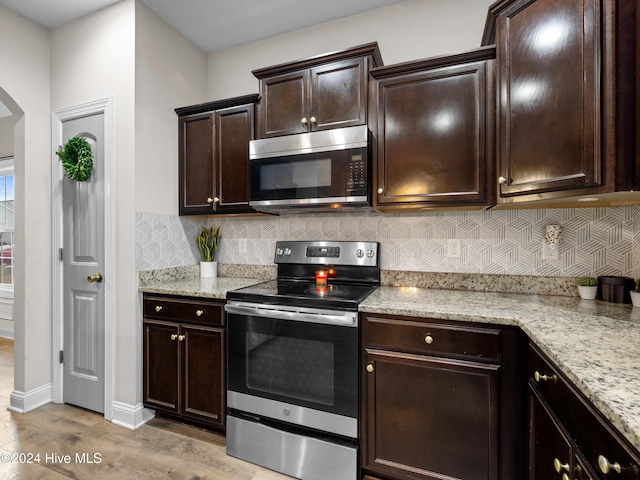 kitchen with light wood-type flooring, stainless steel appliances, dark brown cabinets, and light stone counters