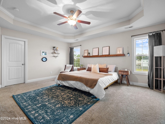 carpeted bedroom with ceiling fan, multiple windows, a tray ceiling, and crown molding