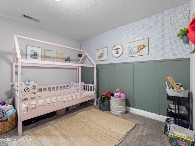 carpeted bedroom featuring a crib and a textured ceiling