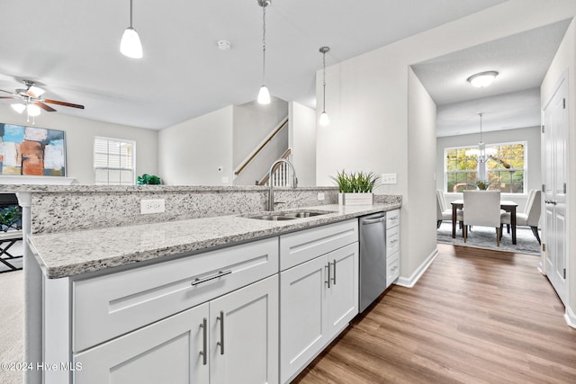 kitchen with light stone countertops, stainless steel dishwasher, sink, white cabinets, and hanging light fixtures