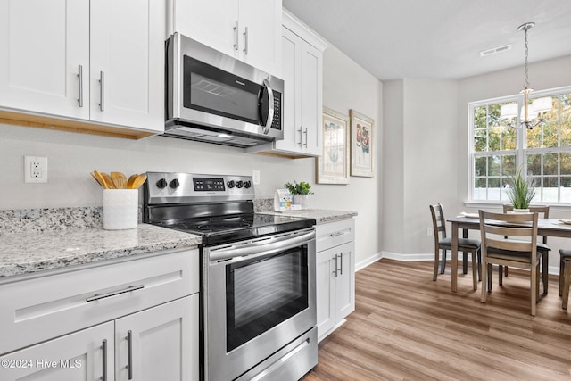 kitchen featuring appliances with stainless steel finishes, light stone counters, decorative light fixtures, a notable chandelier, and white cabinetry