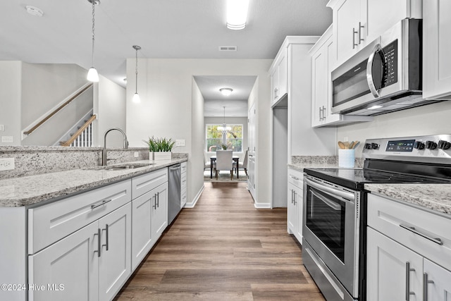 kitchen featuring white cabinetry, sink, light stone countertops, decorative light fixtures, and appliances with stainless steel finishes