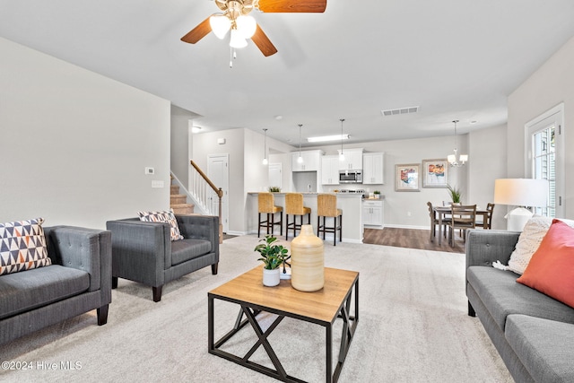 carpeted living room with ceiling fan with notable chandelier