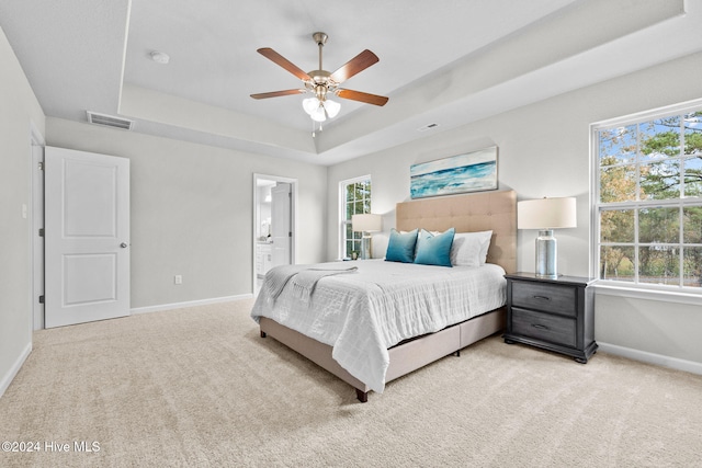 bedroom with ensuite bath, ceiling fan, light carpet, and a tray ceiling