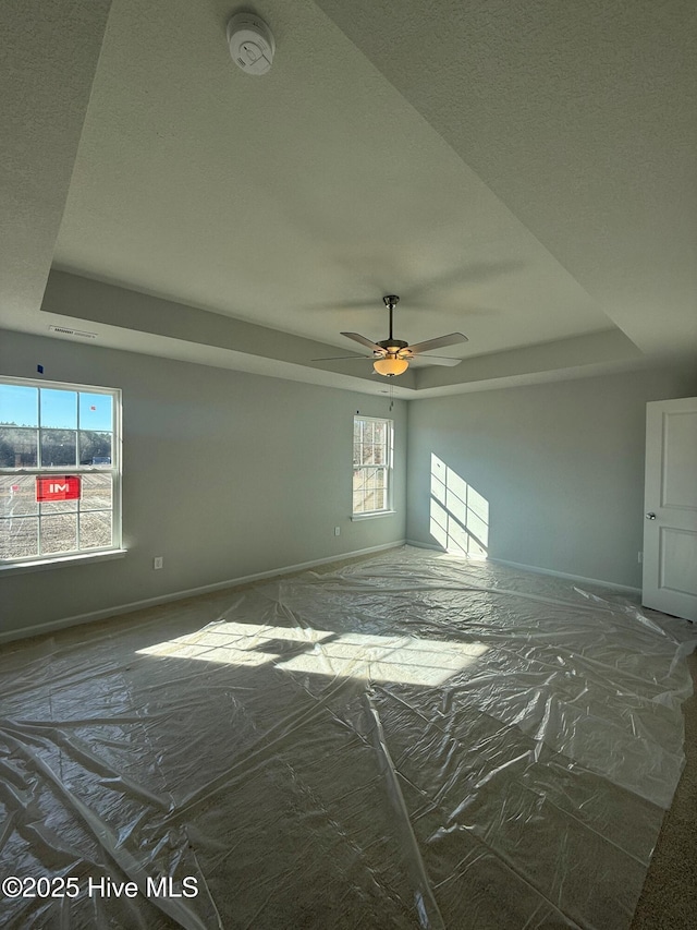 empty room with a raised ceiling, ceiling fan, and a healthy amount of sunlight