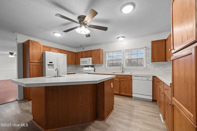 kitchen with sink, tasteful backsplash, a kitchen island with sink, white appliances, and light hardwood / wood-style floors