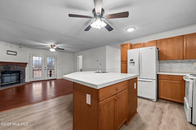 kitchen with sink, a textured ceiling, light hardwood / wood-style flooring, a kitchen island, and white appliances