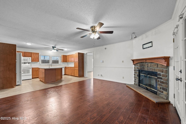 unfurnished living room featuring a stone fireplace, a textured ceiling, ceiling fan, and light wood-type flooring