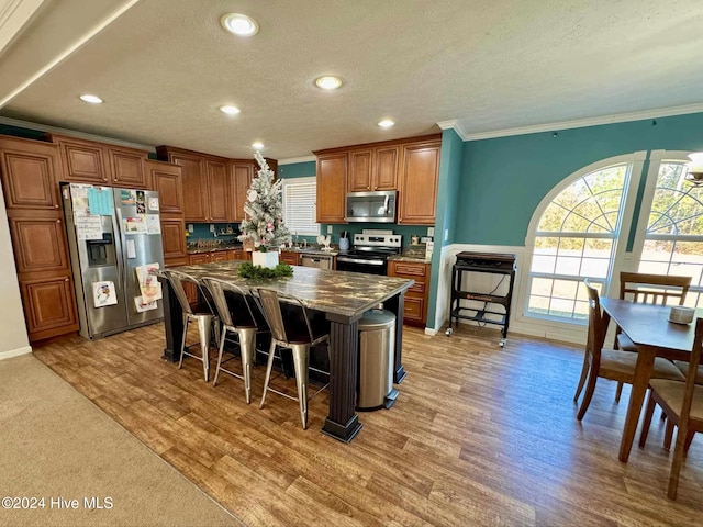 kitchen with a center island, stainless steel appliances, light hardwood / wood-style floors, a breakfast bar area, and ornamental molding