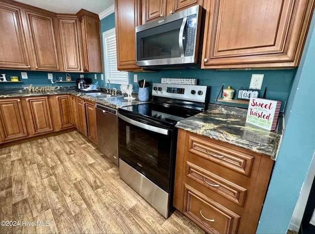 kitchen with sink, stainless steel appliances, dark stone counters, light wood-type flooring, and ornamental molding