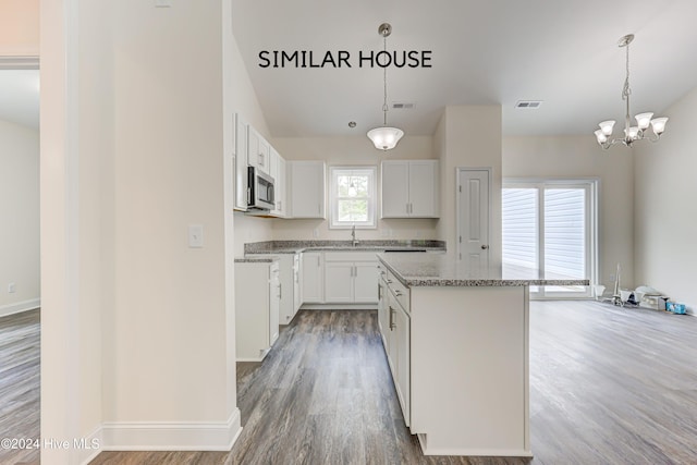 kitchen with light stone countertops, hanging light fixtures, a kitchen island, white cabinets, and hardwood / wood-style flooring