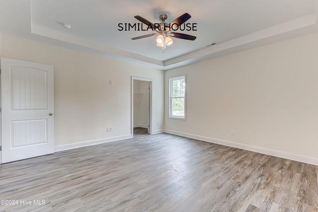 empty room featuring a tray ceiling, ceiling fan, and light hardwood / wood-style flooring