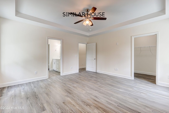 unfurnished bedroom featuring a walk in closet, a tray ceiling, ceiling fan, and connected bathroom