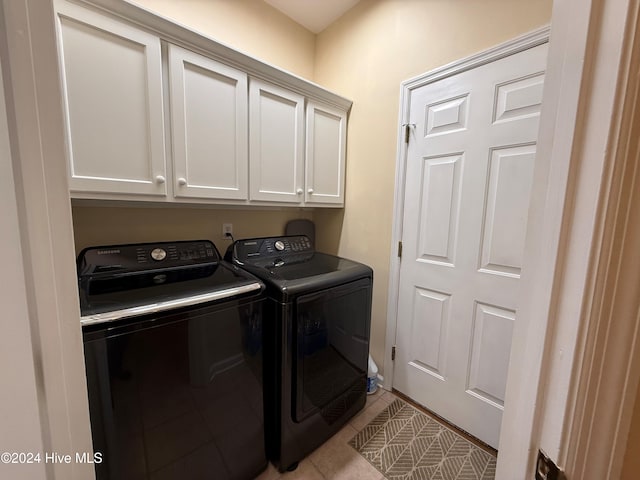 laundry area featuring washing machine and dryer, light tile patterned floors, and cabinets