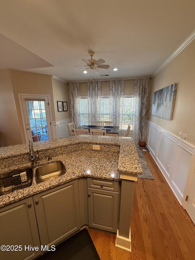 kitchen featuring plenty of natural light, light stone counters, ornamental molding, and light hardwood / wood-style flooring