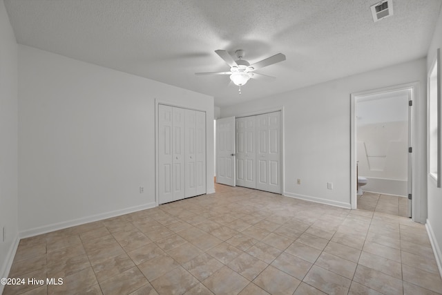 unfurnished bedroom featuring a textured ceiling, two closets, ceiling fan, and connected bathroom