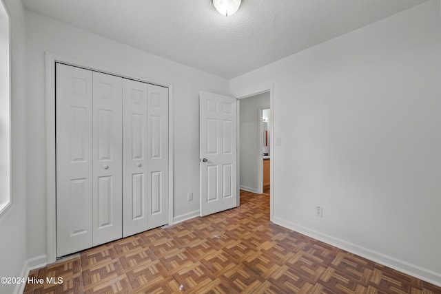 unfurnished bedroom featuring a closet, dark parquet floors, and a textured ceiling