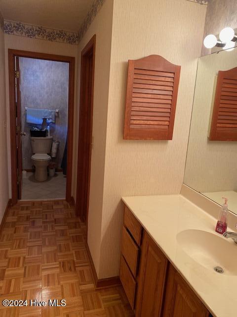 bathroom with vanity, toilet, and parquet flooring