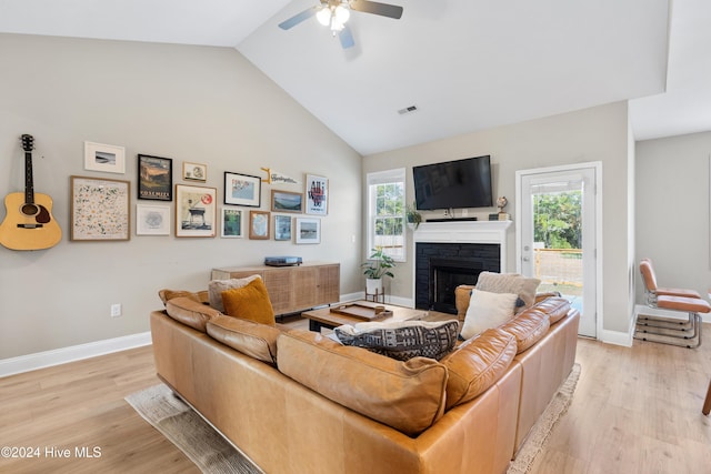 living room featuring plenty of natural light, ceiling fan, a stone fireplace, and light wood-type flooring